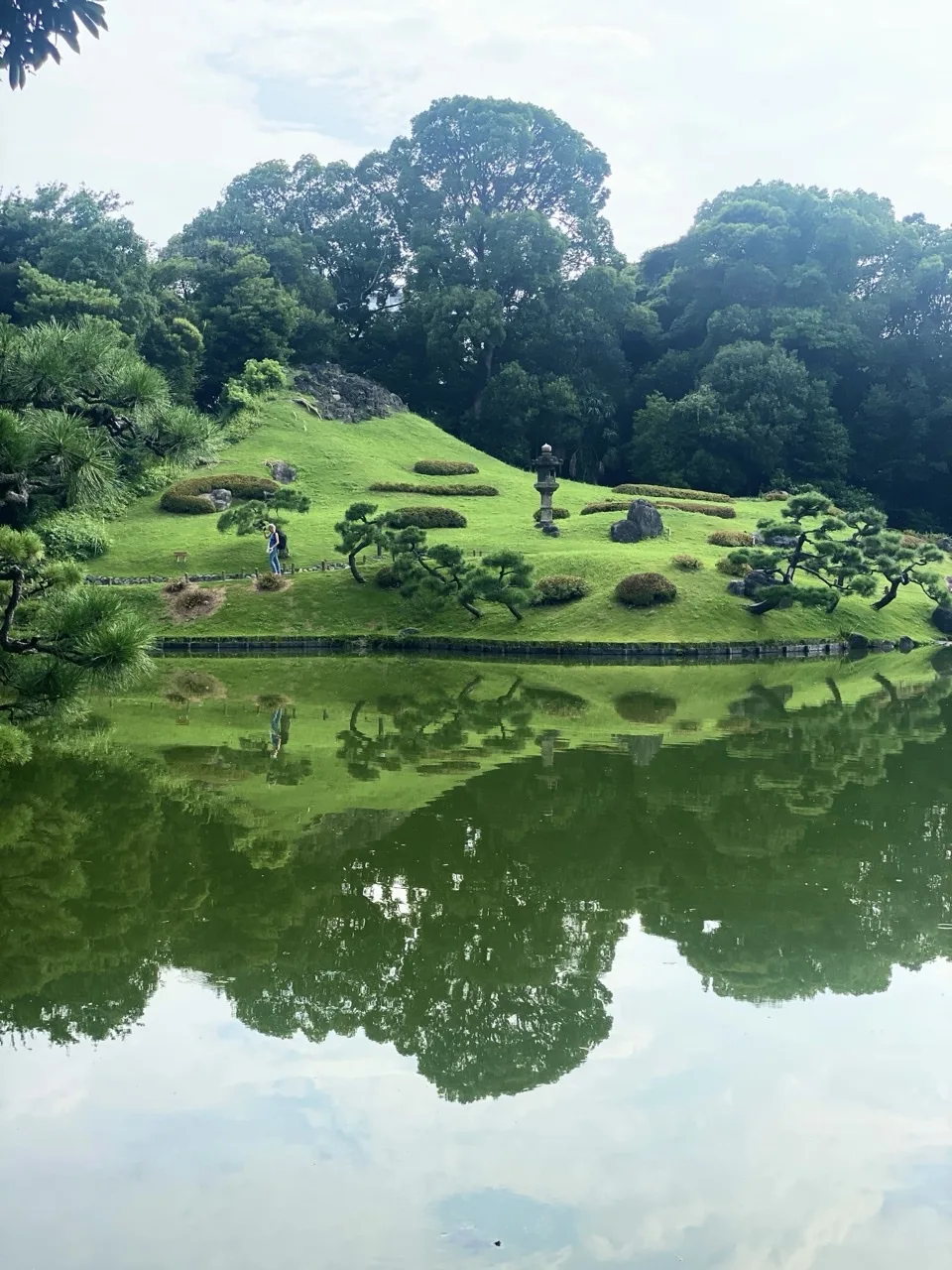 池に浮かぶ中の島に松と石灯籠が配され、水面に景色が鏡のように映る。島の上を人が歩く。