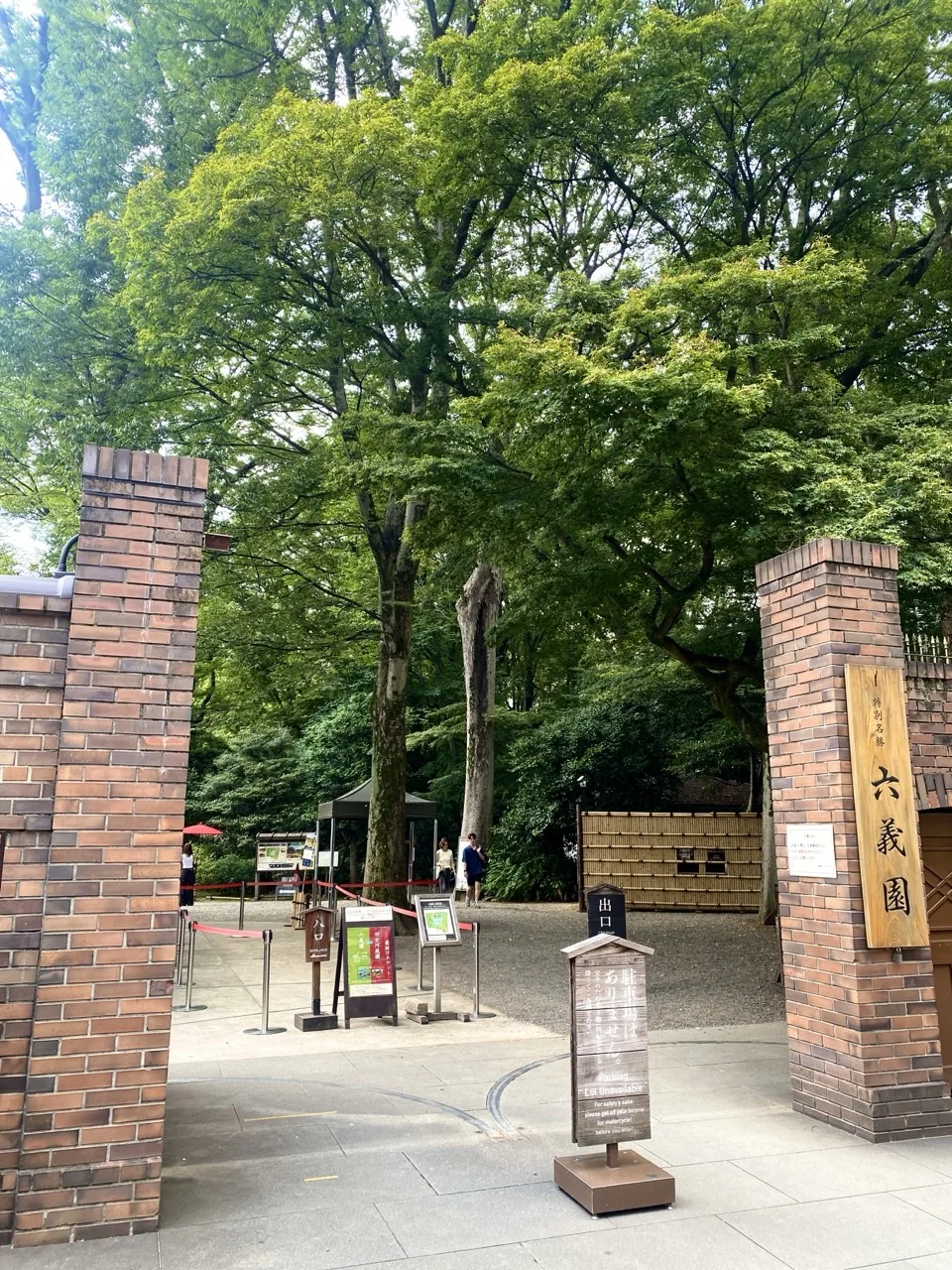 赤煉瓦の門柱が二本並び、奥に木立と園路が見える六義園の入口。
