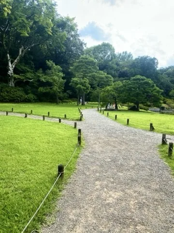 広い芝生の中を緩やかにカーブする砂利道。両脇に木立が見える。