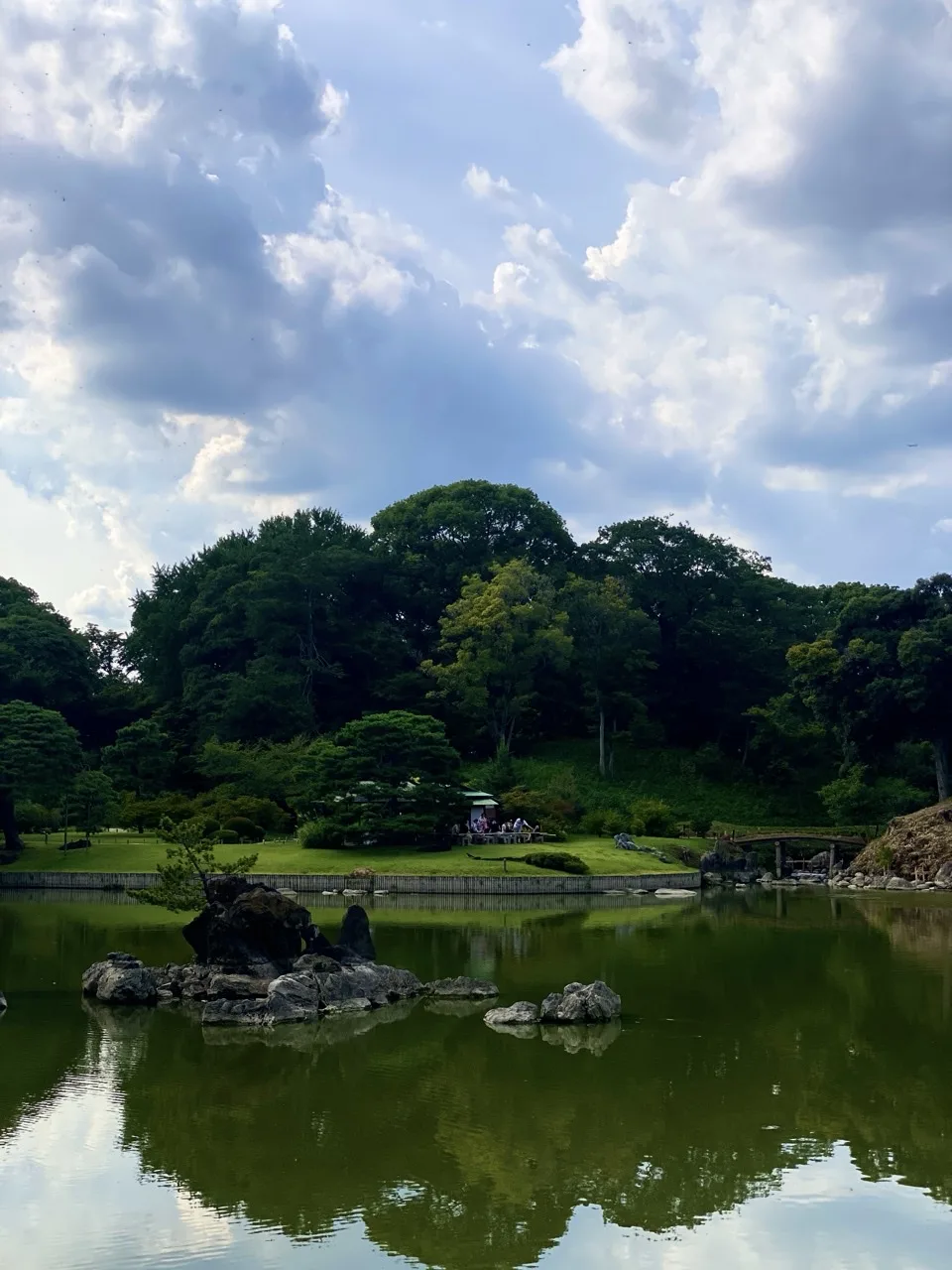 六義園の池を対岸から見た写真。水面に木々と石組みが映り込んでいる。