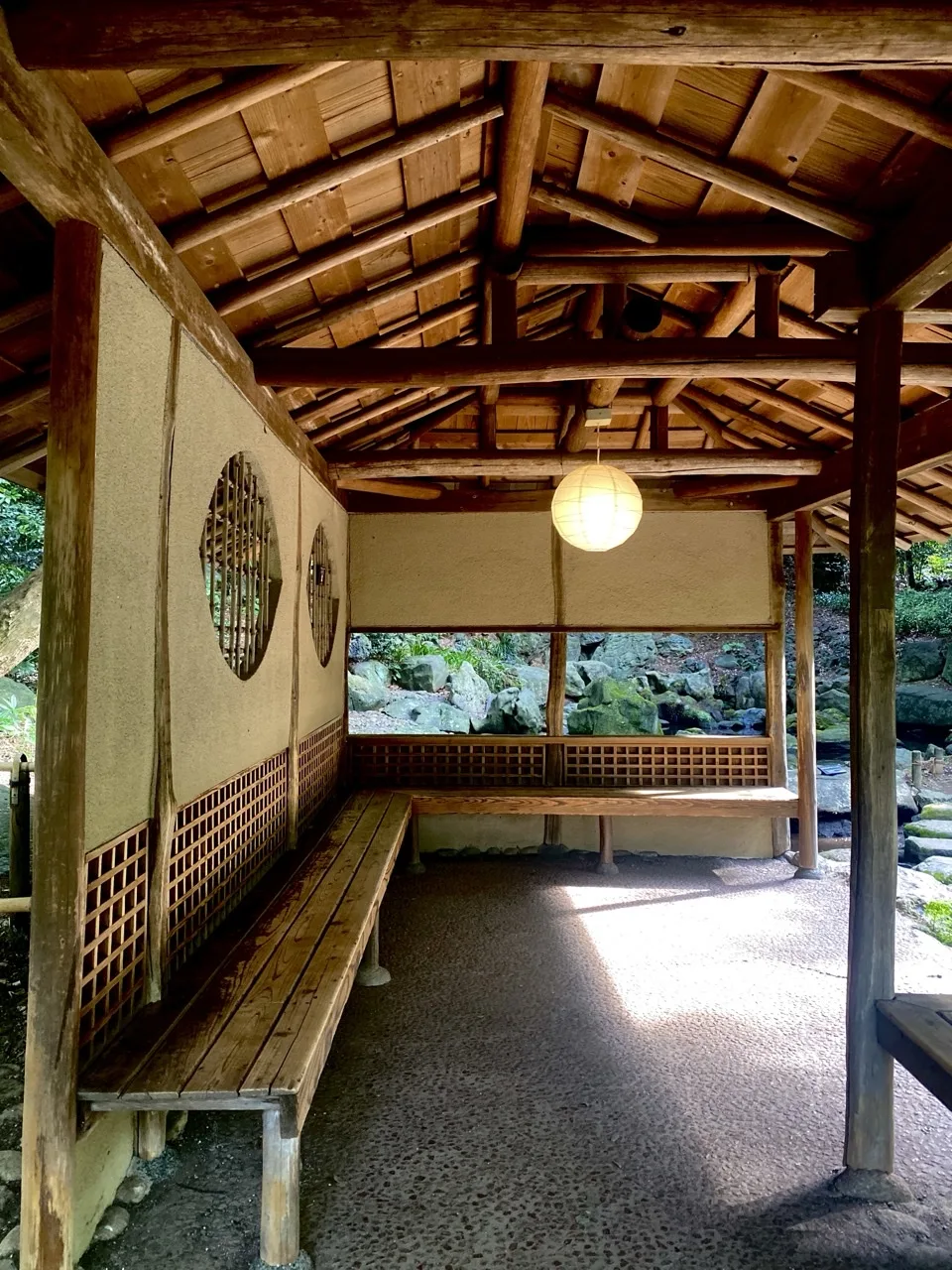 茅葺屋根の東屋の内部から、柱の間に庭園の緑を見た写真。行灯が灯る。