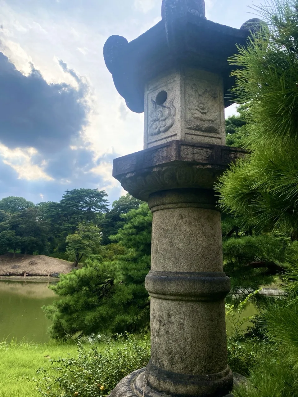 池のほとりに立つ石灯籠を撮った写真。奥に対岸の緑が見える。