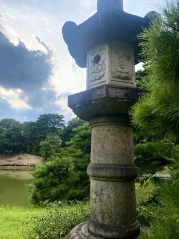 池のほとりに立つ石灯籠を撮った写真。奥に対岸の緑が見える。