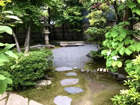 苔の地面に平たい飛石が点々と続き、その先に白い砂利敷きの面と石灯籠、竹垣がある。左右は低木と若葉の楓。