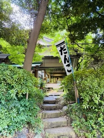 木立に挟まれた石段が上へ続き、その先に軒の低い茶屋がある。右手に「だんご」と書かれた白い幟が高く立つ。