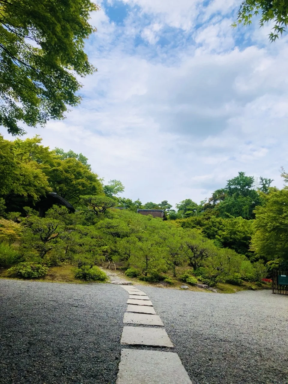 広い砂利敷きの面を、四角い切石が一列に並んで奥へ続く。その先は刈込まれた松の斜面で、上半分は雲の多い明るい空。