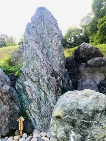 緑がかった大きな立石を中心に、黒い溶岩石や白い筋の入った緑色の岩が組まれている。